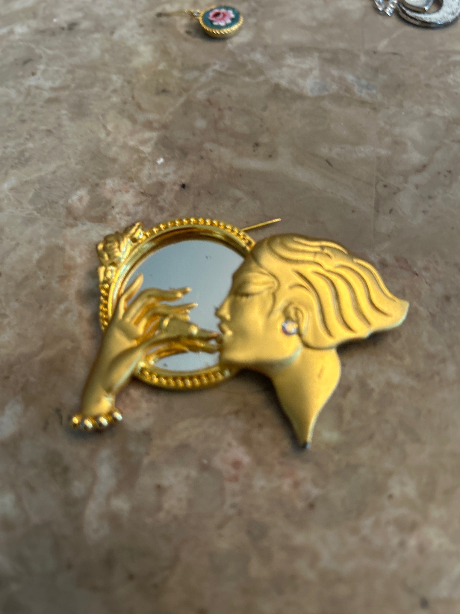 Submitted photo of Gold-tone figural brooch depicting a woman applying lipstick in a mirror